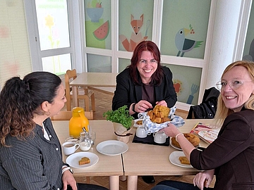 Drei Frauen sitzen an einem Tisch im neuen Kinderrestaurant des Kindercampus Freiburg. Sie unterhalten sich und essen Kuchen. Von links nach rechts: Julia Tapai, Monika Stein und Nina Bardehle.