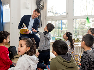 Den Sozialraum einbinden - FRÖBEL-Kindergärten und Horte sind gut vernetzt und binden z.B. Familienangehörige als Vorlesepatinnen und -paten ein. Hier liest der Neuköllner Bezirksbürgermeister Martin Hikel eine Geschichte von Janosch vor.  (Fotocredits: FRÖBEL e.V./Bettina Straub)